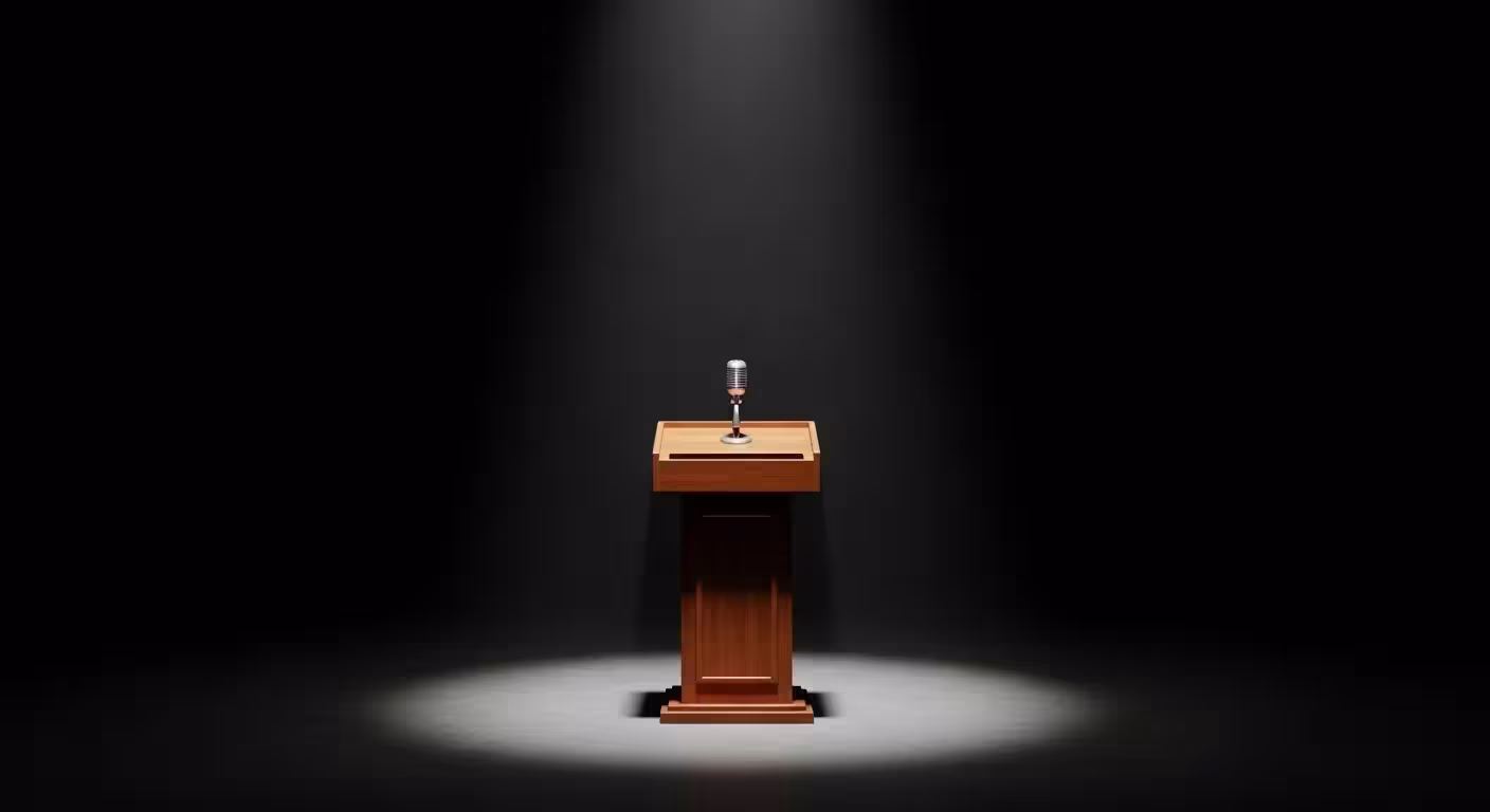 An empty podium and microphone on a stage, lit by a single spotlight in a dark, empty auditorium.