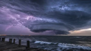 A dramatic wide-angle photo of a massive tropical storm system forming over a dark ocean at twilight with turbulent waves.